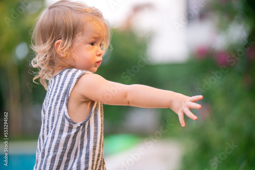 Portrait of toddler in nature. Cute girl in a striped dress looks far away, stretches