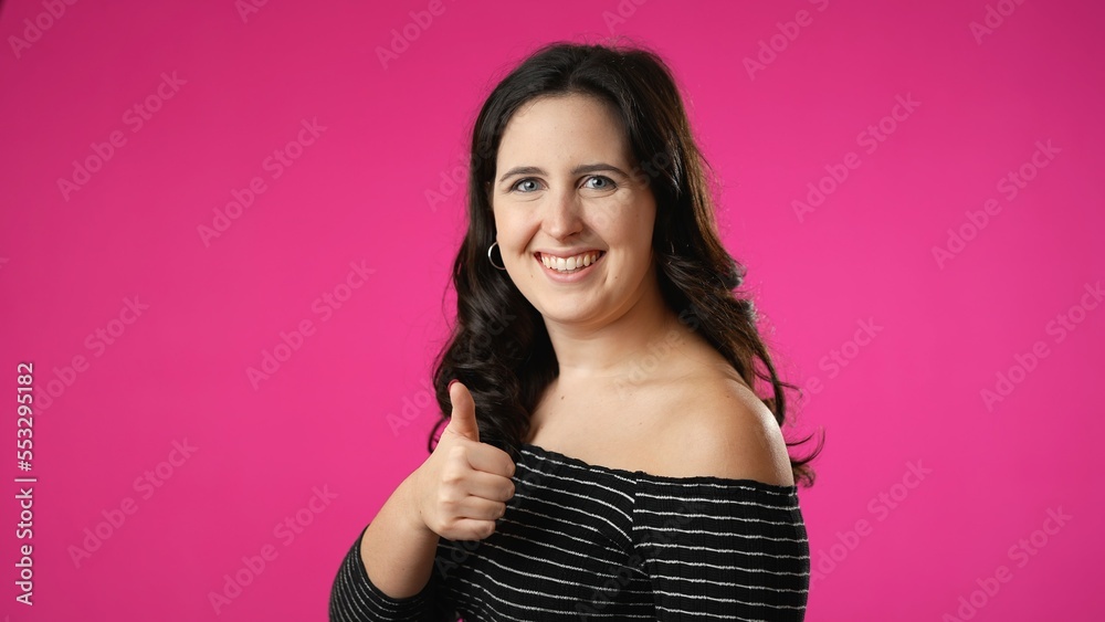 Pretty brunette young woman 20s 30s turn around camera showing thumbs up like gesture portrait isolated on pink background in studio.