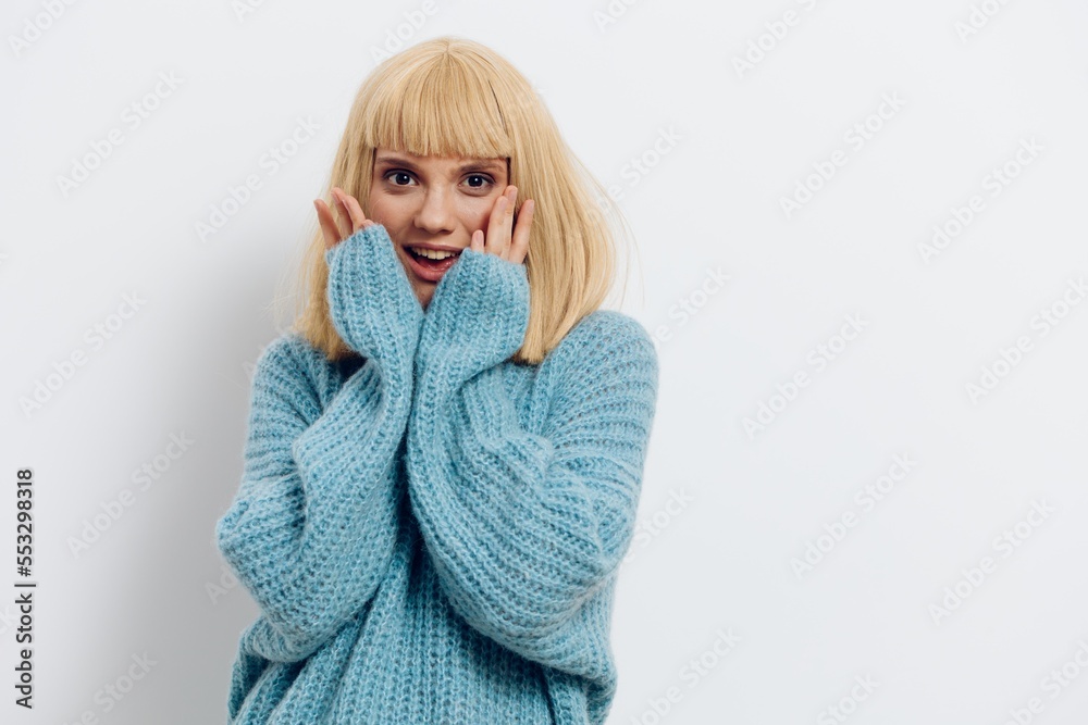 a close horizontal photo of a beautiful, sweet, pleasant woman in a stylish light blue sweater, smiling happily standing on a light background and holding her hands near her face a close horizontal photo of a beautiful, sweet, pleasant woman in a stylish light blue sweater, smiling happily standing on a light background and holding her hands near her face