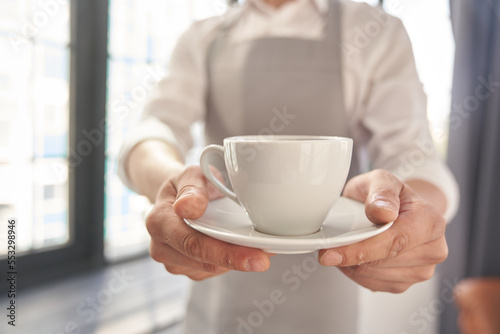 Your coffee, please. Cropped image of a man holding a cup of good coffee against the background of a window with space to copy. High quality photo