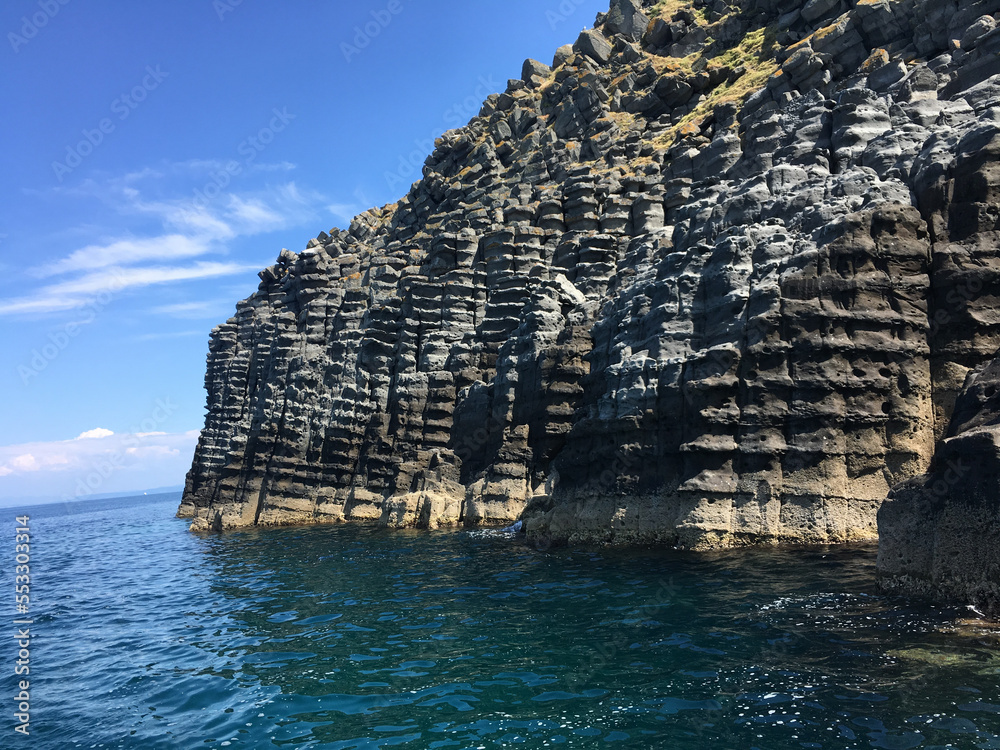 The volcanic rock formations along the sea strip on Imbros island of Gökçeada are called Cheese cliffs. Canakkale, Turkey. Rocky mountain formations stacked on top of each other by the sea and wind