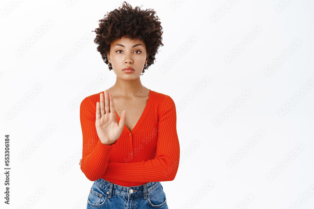 Portrait of serious Black girl shows stop gesture, disapprove smth, rejects and prohibits, stands over white background Portrait of serious Black girl shows stop gesture, disapprove smth, rejects and prohibits, stands over white background