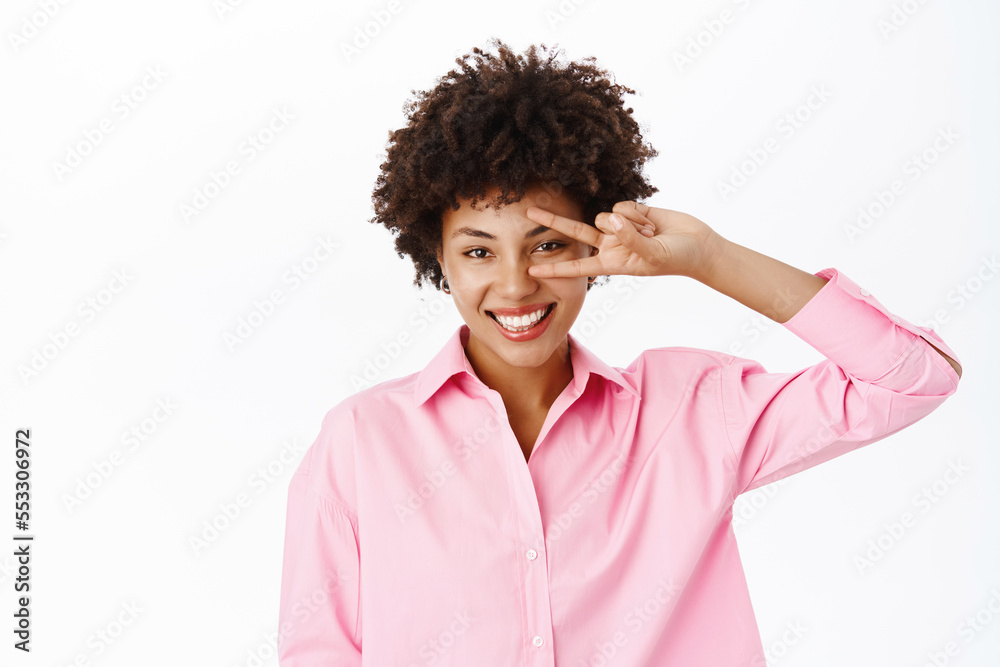 Portrait of beautiful modern woman in pink blouse, shows beautiful white smile, poses with peace gesture over white background Portrait of beautiful modern woman in pink blouse, shows beautiful white smile, poses with peace gesture over white background