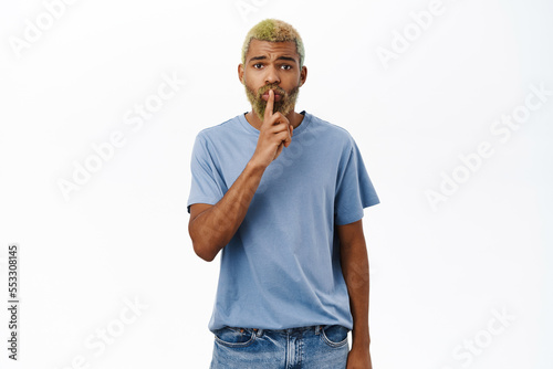 Concerned guy asks to keep quiet, shares secret, shows shh shush gesture, taboo sign, stands over white background