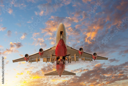 Plane with extended landing gear goes on take off at sunset. Landing plane at sunset cloudy moody sky.