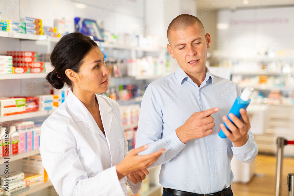 Female specialist is helping male client choose medicine in pharmacy