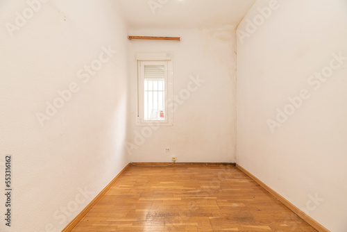 Empty living room with white painted walls  small white aluminum plate window with bars and loose floating oak flooring