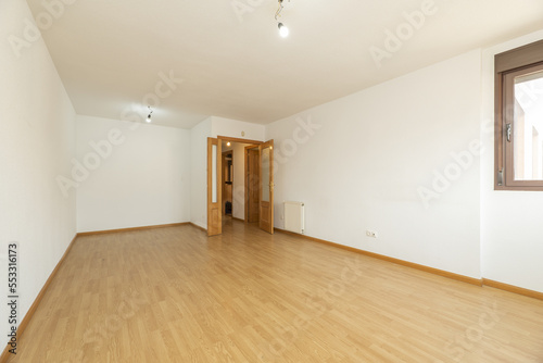 Empty living room with oak double doors and matching laminated flooring finished with skirting of the same material