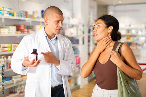 Male pharmacist proposing medicine to oriental woman who complaining about sore throat.