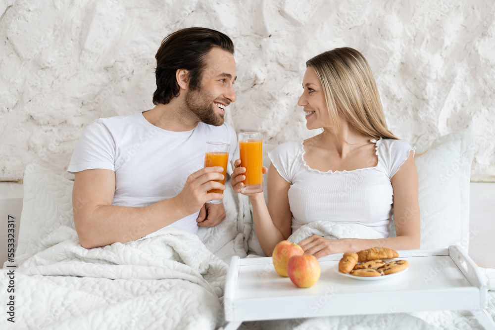 Loving caucasian couple having breakfast in bed together, spending honeymoon morning at modern hotel Loving caucasian couple having breakfast in bed together, spending honeymoon morning at modern hotel