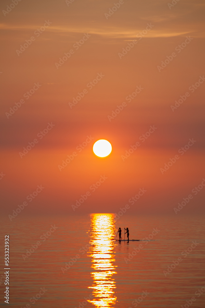 Two person, couple riding on Stand up paddles on the Baltic Sea into the sunset