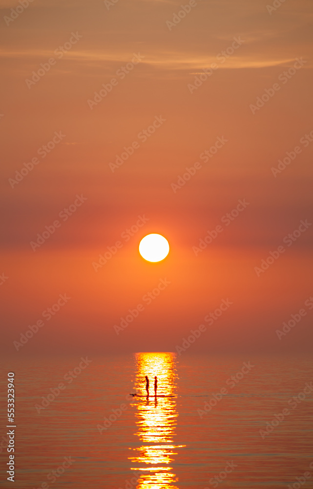 Two person, couple riding on Stand up paddles on the Baltic Sea into the sunset