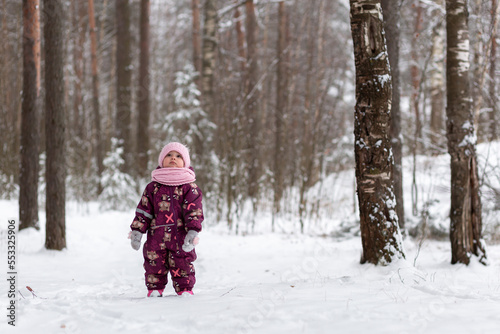 A little girl looks up in a winter snowy forest, New Year holidays, winter, snow.