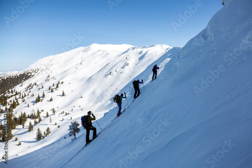 a team of ski tourists is actively climbing up a mountain range with overhanging snow cornices