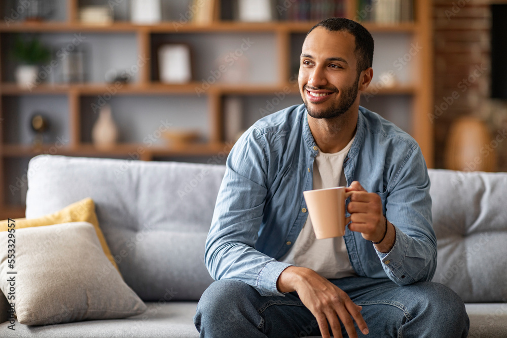 Portrait of handsome african american man resting on couch with cup of coffee