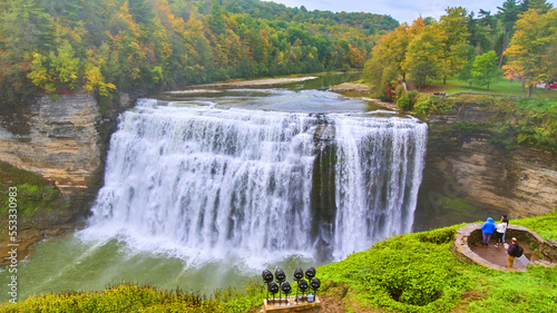 Huge raging waterfall in river through canyon with colorful foliage and tourists admiring from vista