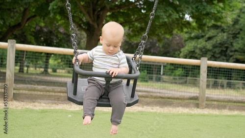 Funny Little Younger Newborn Infant Brother Boy On Swing. Baby Playing On Playground. Summer time outside. Kids Entertainment, Childhood, Child Development, Happy Family Concept