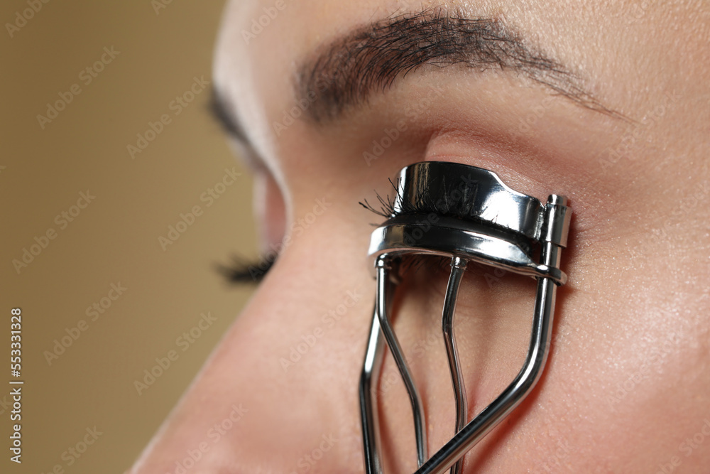 Woman using eyelash curler on beige background, closeup. Space for text