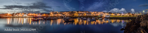 Portrush, Panorama of a small port town with a little harbour, boats and houses during a late summer night, blue hour, lights switched on
