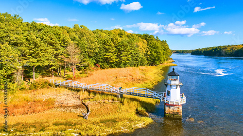 Aerial of small lighthouse Doubling Point on Maine Coast with fall foliage and warm light photo