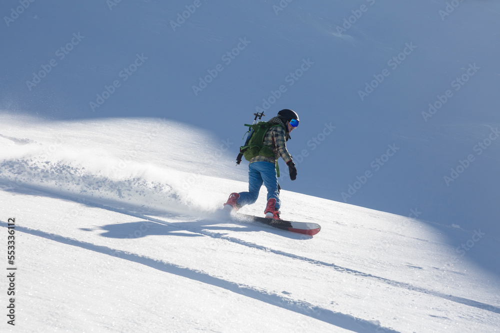 A snowboarder descends leaving a wave of snow, a play of shadow and light