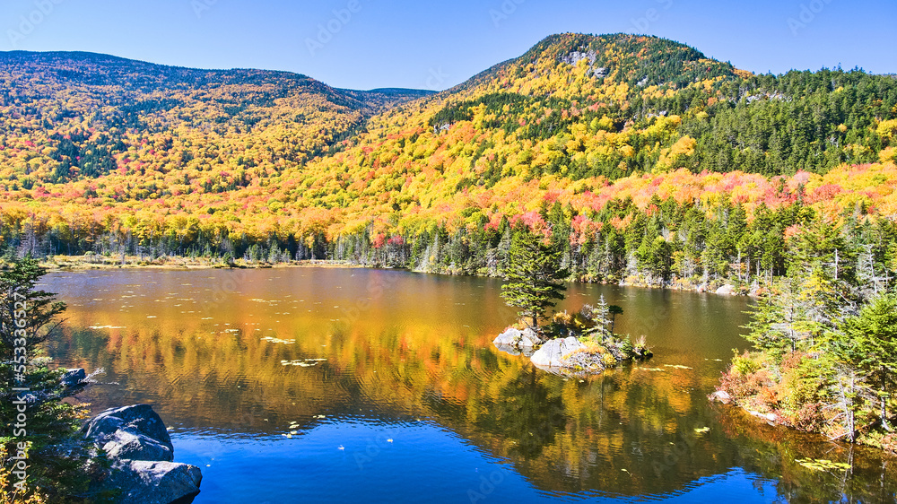 Lake in New Hampshire reflecting colorful peak fall mountains and lone rocky island with pine tree