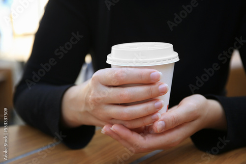 Woman with cardboard cup of coffee at table, closeup