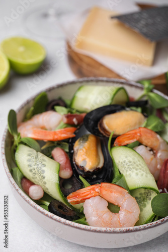Bowl of delicious salad with seafood on light grey table, closeup