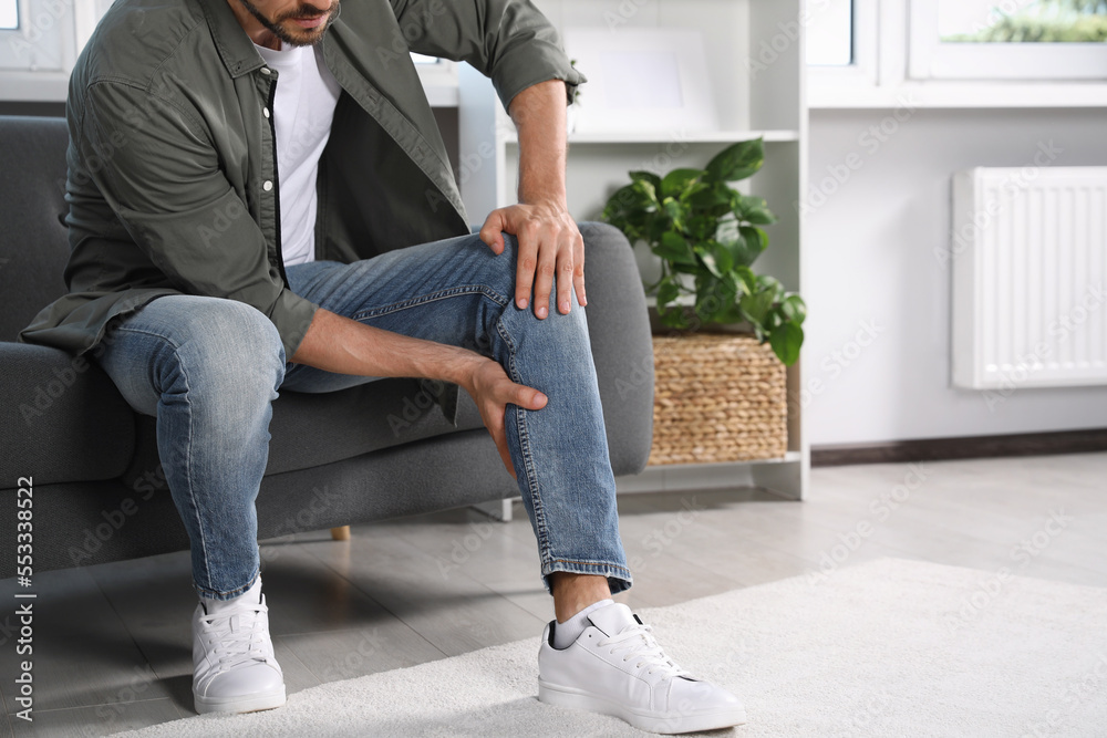 Man suffering from pain in leg on sofa at home, closeup. Space for text Man suffering from pain in leg on sofa at home, closeup. Space for text