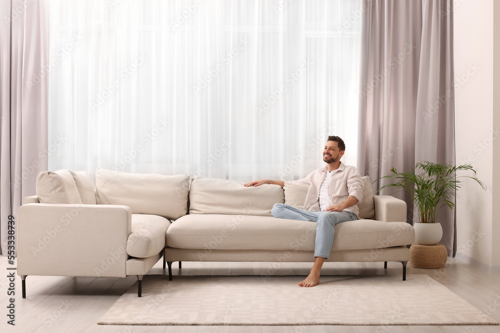 Happy man resting on sofa near window with beautiful curtains in living room Happy man resting on sofa near window with beautiful curtains in living room