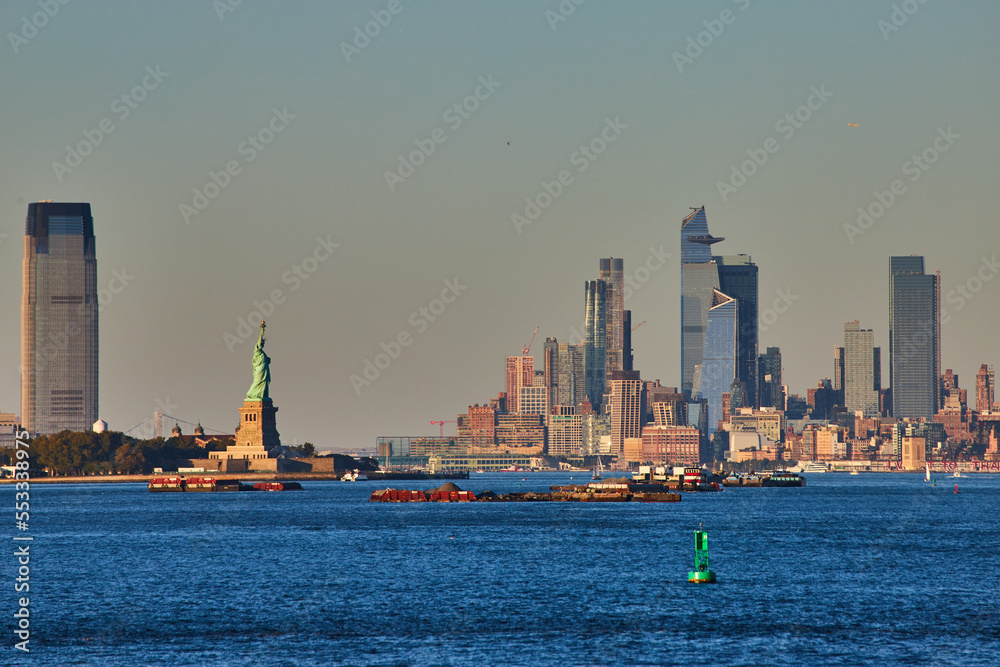 Statue of Liberty in golden light from ferry with view of New York City skyline skyscrapers