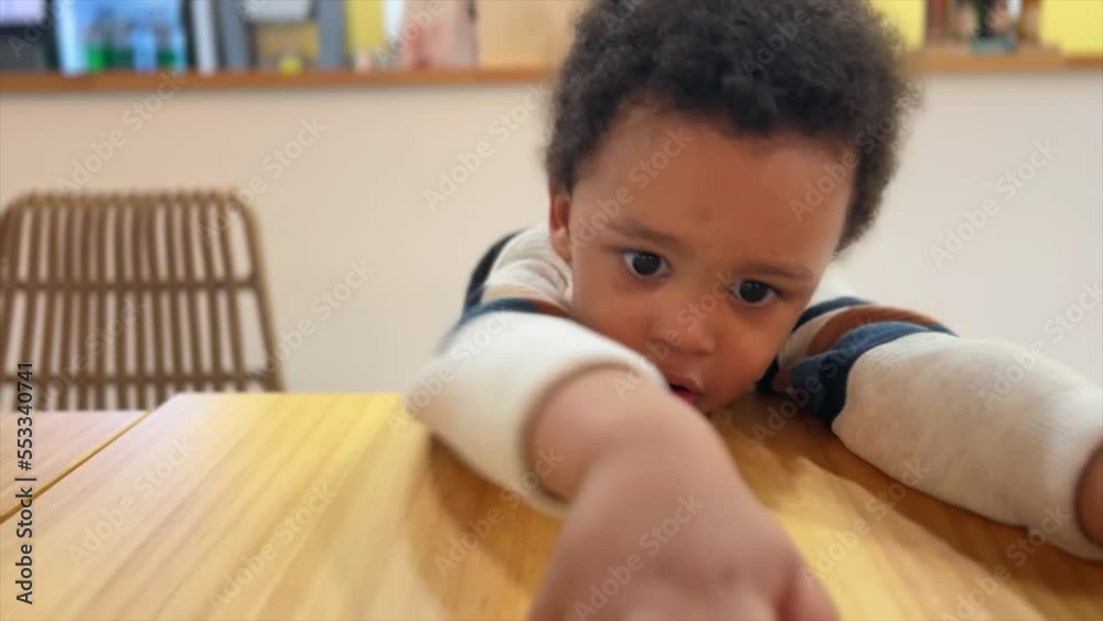 Close view of a cute two-year-old mix raced baby, very expresive black eyes, playing with his toy car on a wood table inside a cafeteria. Close view of a cute two-year-old mix raced baby, very expresive black eyes, playing with his toy car on a wood table inside a cafeteria.