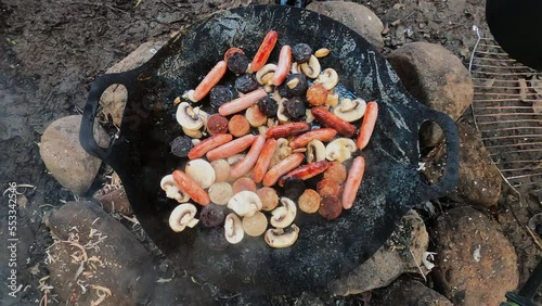 Overhead view as sausages and mushrooms fry in Petromax Fire Bowl pan photo