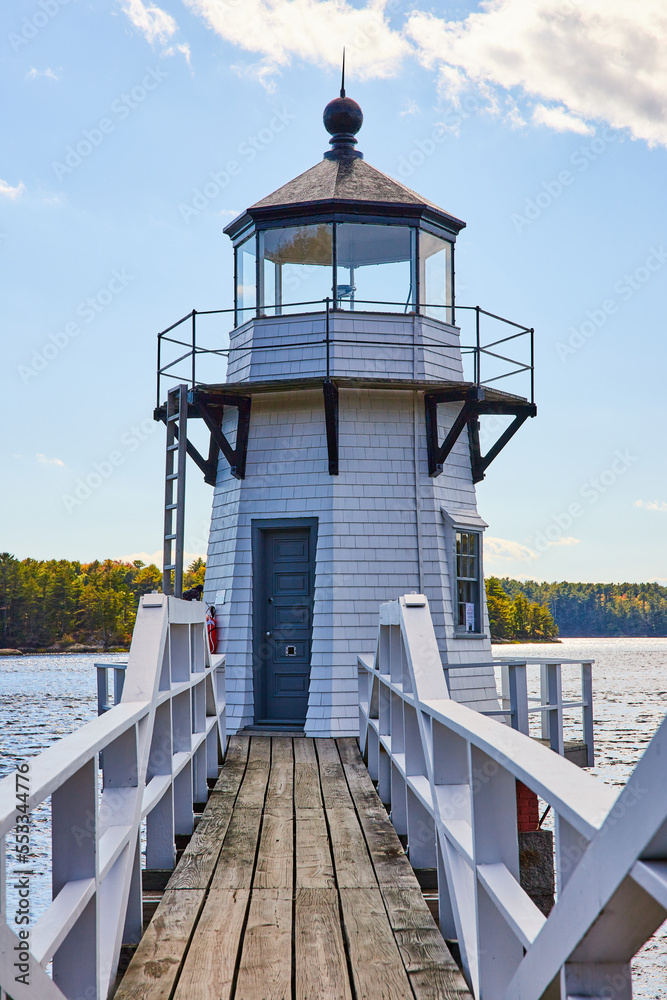 Boardwalk with railing leads to small white lighthouse on Maine river