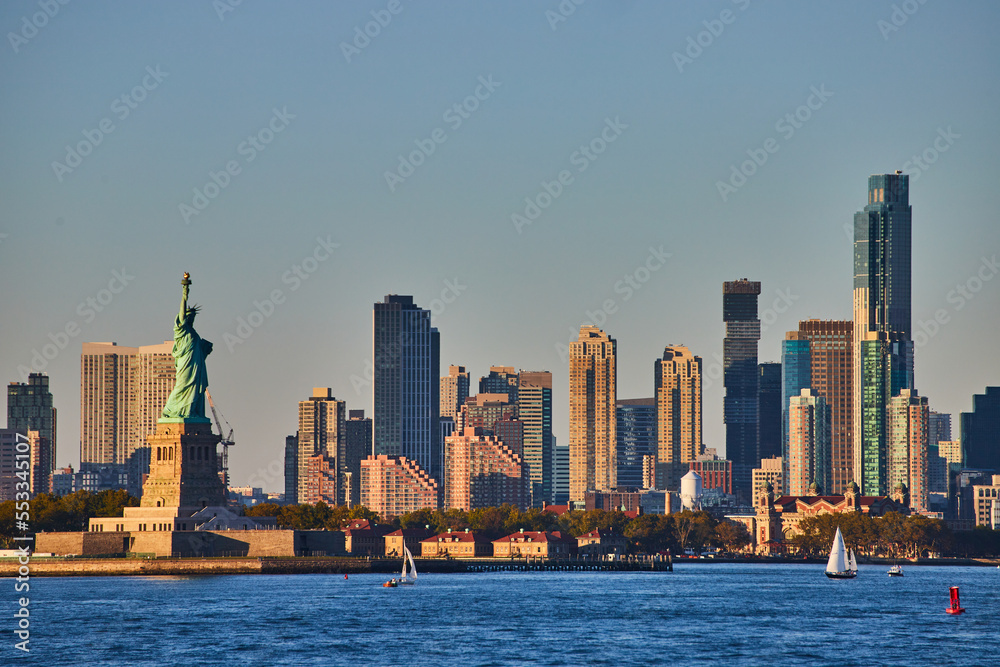 Statue of Liberty with skyscrapers surrounding from waters in golden light
