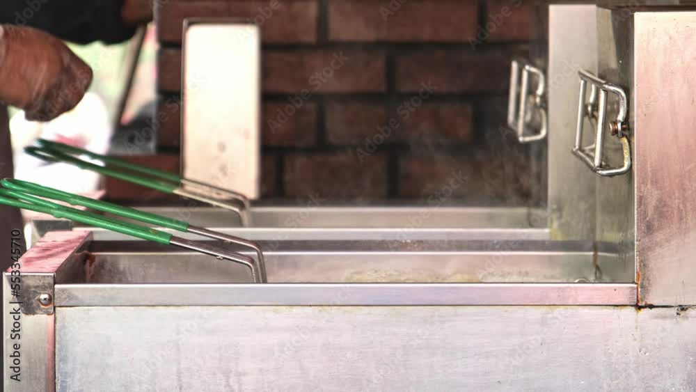 Fried Potato Production Process. Multiple Pieces of fried potato are placed in the fryer net. Cooking the fried potato in the burning hot oil in the Deep Fryer Equipment. Modern Fast Food Industry.

