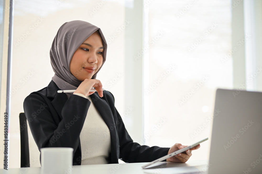 Attractive Asian Muslim businessman using laptop, looking at laptop screen, working in the office.