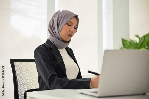 Professional Asian Muslim businesswoman concentrating on her business tasks, working in office