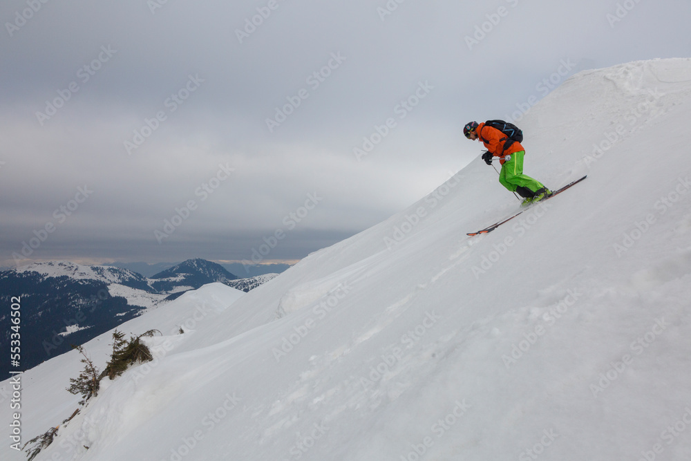 A freerider skier descends a steep slope against the background of mountain ranges