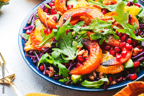 Fresh pumpkin salad with red cabbage, avocado, lettuce, arugula, pomegranate and nuts. Vegan healthy eating, slow comfort food. White table background. Top view