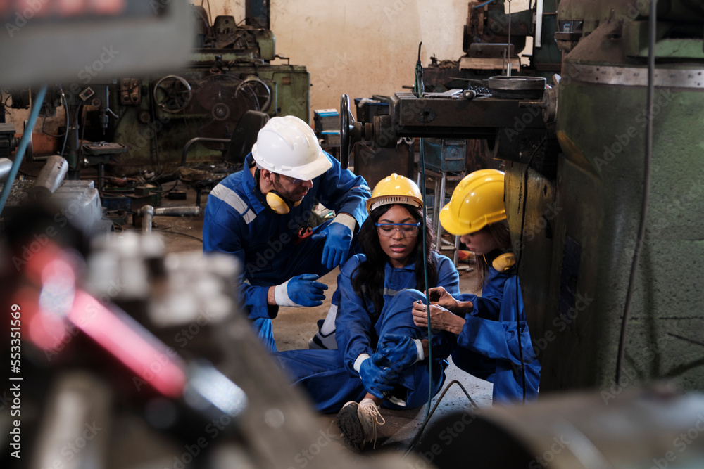Painful accident in industrial production metalwork, African American female worker injured her leg, male engineer and colleague team helped first aid with care at manufacturing machinery factory. Painful accident in industrial production metalwork, African American female worker injured her leg, male engineer and colleague team helped first aid with care at manufacturing machinery factory.