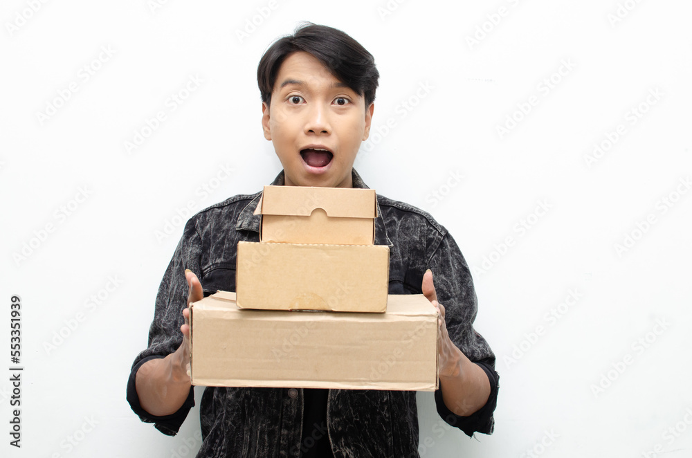 Young Asian man holding package over white background, smiling and excited. Concept of delivery courier and shipping services Young Asian man holding package over white background, smiling and excited. Concept of delivery courier and shipping services