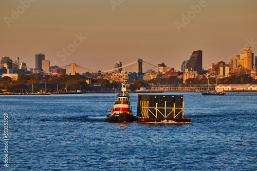 Small industrial ship pulling shipping containers from side in industrial New York City golden hour