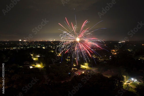 Aerial view of bright fireworks exploding with colorful lights over suburban houses in residential area on US Independence day holiday