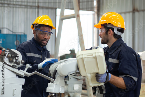 Two engineer man working with machine robot automatic together at factory, technician maintenance and improvement while examining ai of robot and control with remote, industry and innovation concept.