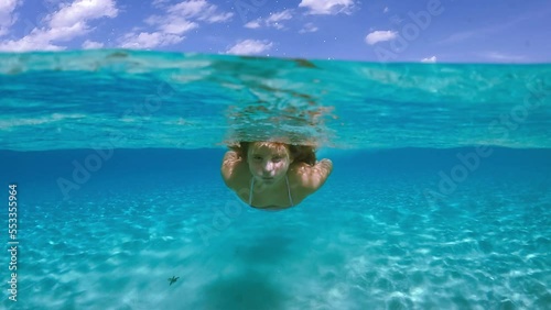 Child girl swims toward camera beneath sea water surface of Saleccia exotic beach in Corsica island, France. Waterline slow motion view photo