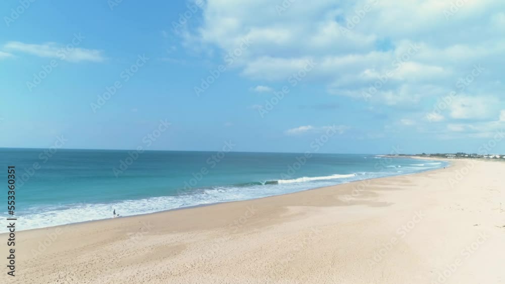Aerial panning view from sand beach to blue sea water over person walking a dog Aerial panning view from sand beach to blue sea water over person walking a dog