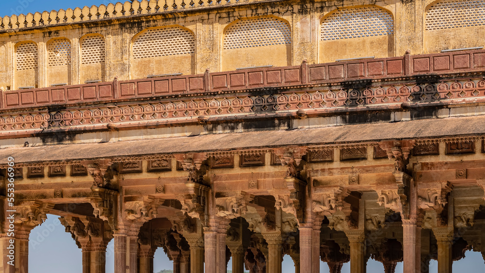 Details of the architecture of the ancient Amber Fort. A colonnade with carved capitals, a wall with ornaments, barred windows are visible. India. Jaipur