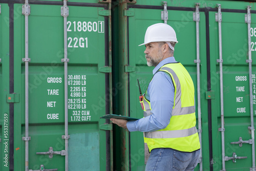 Foreman wearing safety uniform and holding clipboard and pen for inspection container.