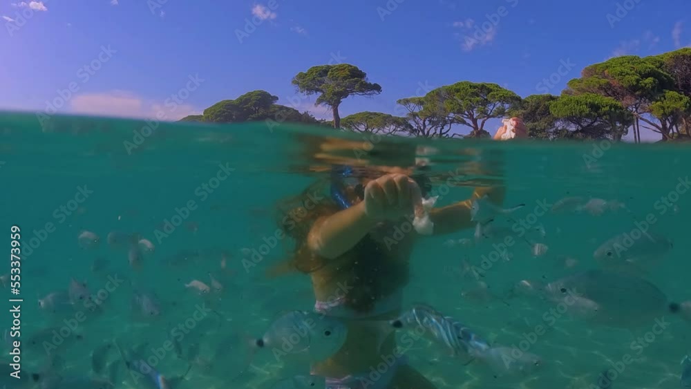 Half underwater scenic view of a adorable little redhead girl with diving mask surrounded by school of fish feeding them with bread. Slow motion Half underwater scenic view of a adorable little redhead girl with diving mask surrounded by school of fish feeding them with bread. Slow motion